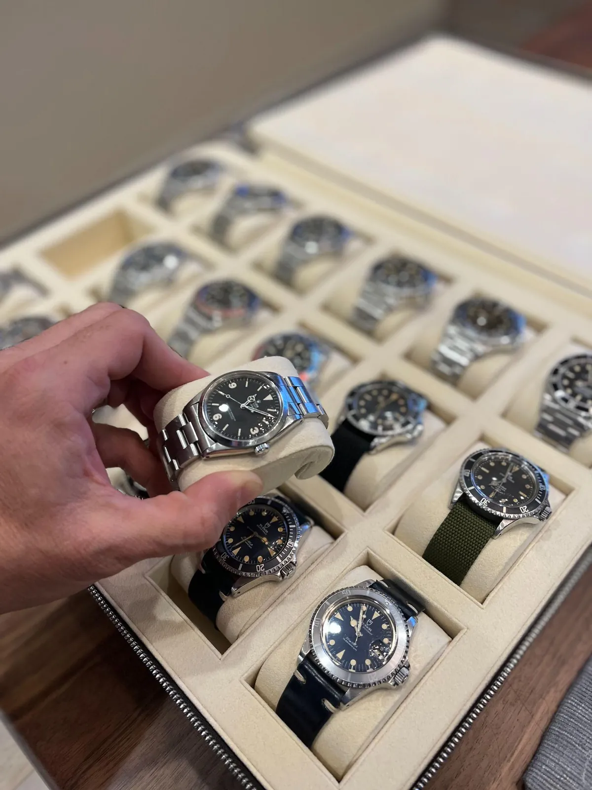 A hand lifts a wristwatch from a tray of watches